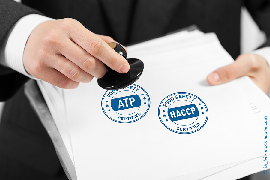 Das Bild zeigt, wie jemand die ATP- und HACCP-Logos auf ein Blatt Papier stempelt