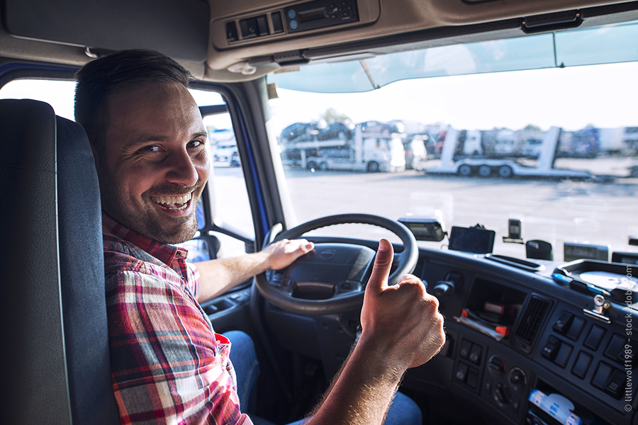 Ein Mann sitzt an dem Lenkrad eines LKW, lächelt und zeigt dabei den Daumen hoch