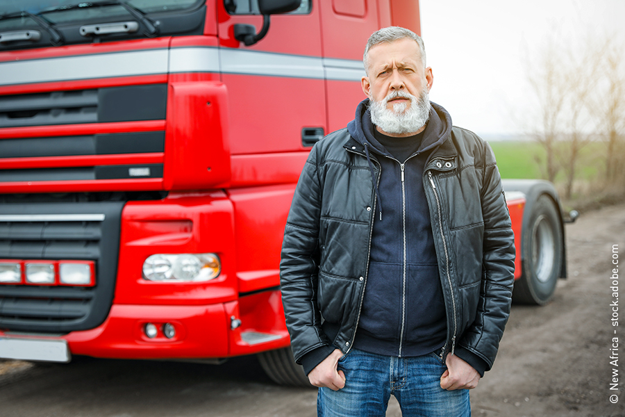 Älterer LKW-Fahrer steht vor seinem Fahrzeug.