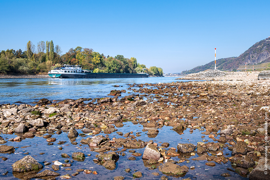 Ein Binnenschiff fährt in Richtung Drachenfels auf dem Rhein, dessen Ufer sehr ausgetrocknet sind.