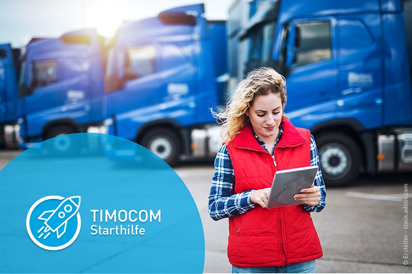 eine-frau-steht-mit-einem-tablet-in-der-hand-vor-blauen-lkw