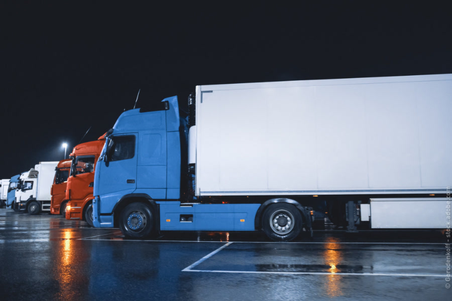 Blauer Lkw auf einem sicheren Parkplatz bei Nacht, umgeben von weiteren Lkw.