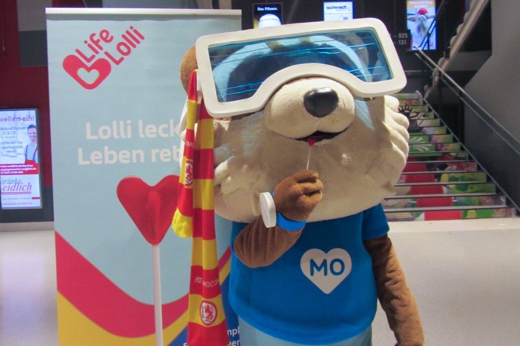 TIMOCOM Maskottchen Mo mit einem Lolli der Typisierungsaktion