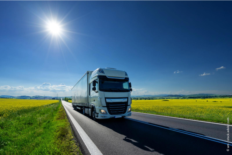 Ein LKW fährt über eine Straße zwischen grüner Landschaft und Feldern.